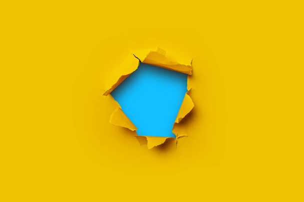 Jasně žlutý natržený papír uvnitř v díře modré lepenkové pozadí - Fotografie, Obrázek