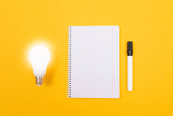 Glowing Power Saving Lamp with Notepad Lying on Yellow Table - Foto, Bild