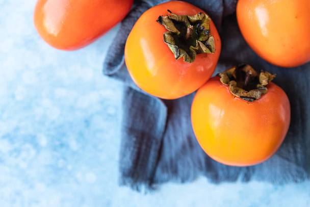 Fresh organic ripe persimmons on blue concrete background. - Foto, afbeelding