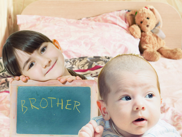 黒板と赤ちゃんの弟の顔を保持している白人の子姉妹  - 写真・画像