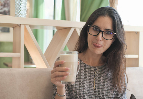 aziatische vrouw draagt bril drinken latte koffie en tonen een tong. tijd doorbrengen in café, ontspannen en plezier hebben. - Foto, afbeelding