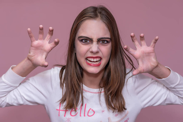 Menina chocada usa maquiagem assustadora, mantém as palmas das mãos levantadas, assusta alguém, celebra o Halloween - Foto, Imagem