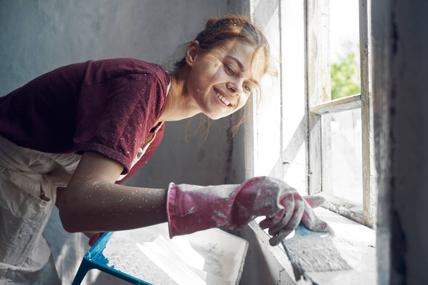 woman with brush paints window sill at home near window interior renovation - Φωτογραφία, εικόνα