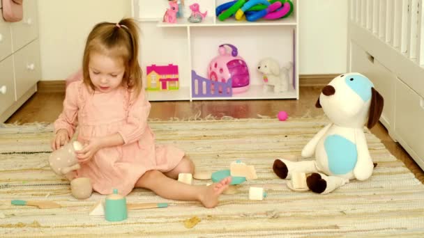 Baby Girl plays in the nursery with toy dishes, pouring tea into cups for her friend teddy dog. A game of tea drinking with fluffy toys - Filmagem, Vídeo
