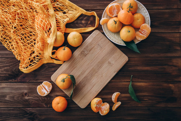 Clementinas frescas, tabla de cortar y bolsa de compras en mesa de madera, vista superior - Foto, Imagen