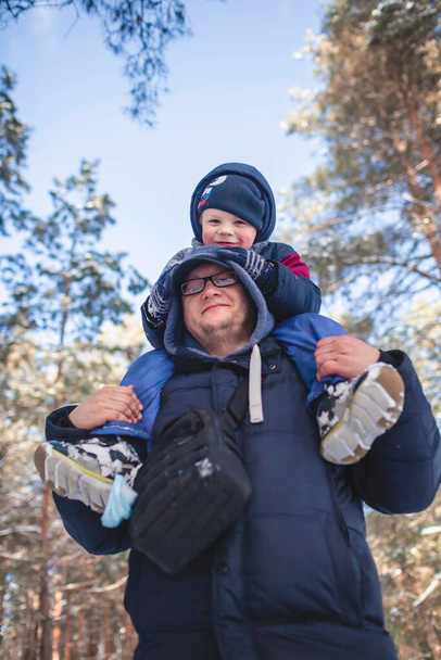Papa draagt zijn zoontje op de schouders zodat hij de tak kan bereiken en sneeuw van de boom kan schudden. - Foto, afbeelding