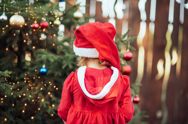 Christmas in july. Child waiting for Christmas in wood in summer. portrait of little girl in red dress decorating christmas tree. winter holidays and people concept. Merry Christmas and Happy Holidays - Foto, Imagem