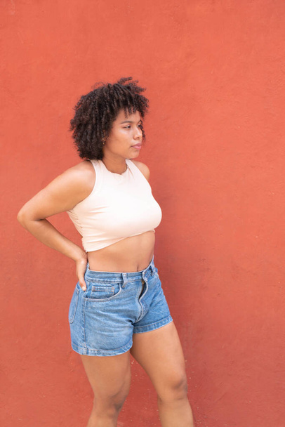 Woman with curly afro hair in front of an orange wall - 写真・画像