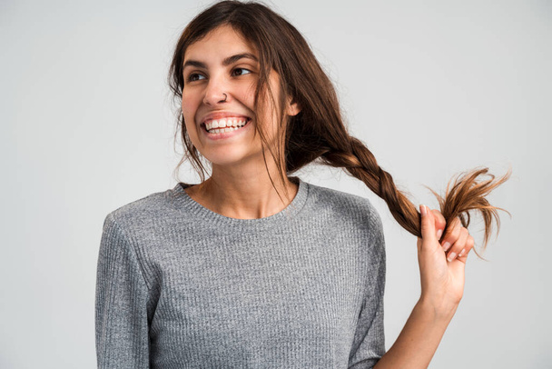 Waist up portrait view of the happy woman holding her braid with toothy smile isolated on a white background. People appearance concept  - Photo, Image