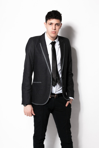 elegant man in black suit leaning against white wall at studio - Photo, Image