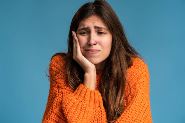 Zubní problémy. Portrét nezdravé ženy stlačující bolavou tvář, trpící akutní bolestí zubů, periodontálním onemocněním, dutinami nebo bolestí čelisti. Vnitřní studio záběr izolované na modrém pozadí - Fotografie, Obrázek