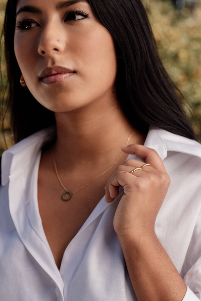 Latin woman with rings and pendant adjusting the collar of her white shirt. model with jewelry. - Photo, image