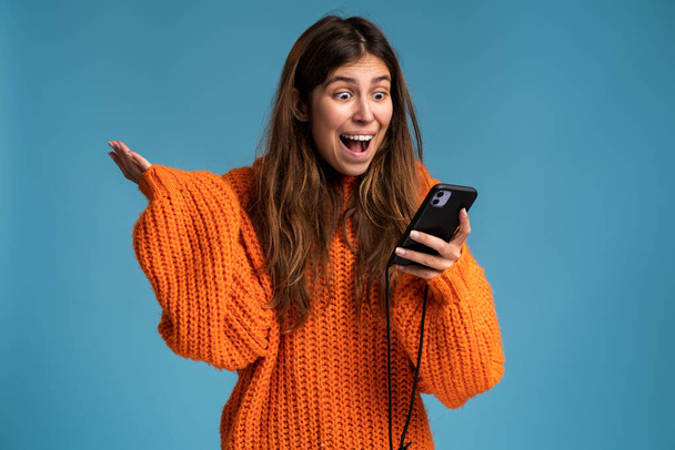 Portrait of excited overjoyed girl rejoicing with mobile phone in hand, celebrating online betting win, successful internet earnings. Indoor studio shot - Photo, Image