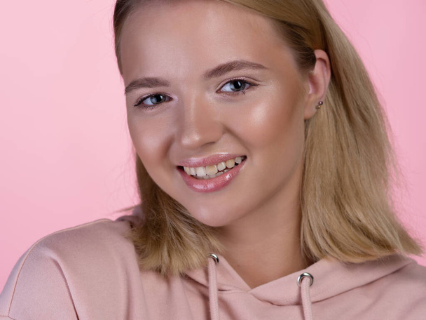 cute young blonde in a pink hoodie is smiling happily. - Fotografie, Obrázek