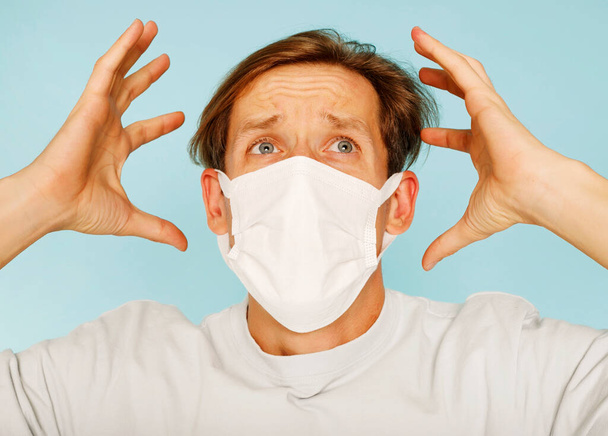 Close up sick young man handsome wearing medical mask and white shirt isolated on blue background. Concept of sickness. - Fotoğraf, Görsel