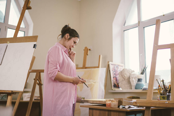 Female artist working in studio. Creative workspace, painting class, easel with canvas, art therapy. Inspiration, creativity, talent, craft concept. Artist studio interior. People, leisure and hobby. - Photo, Image