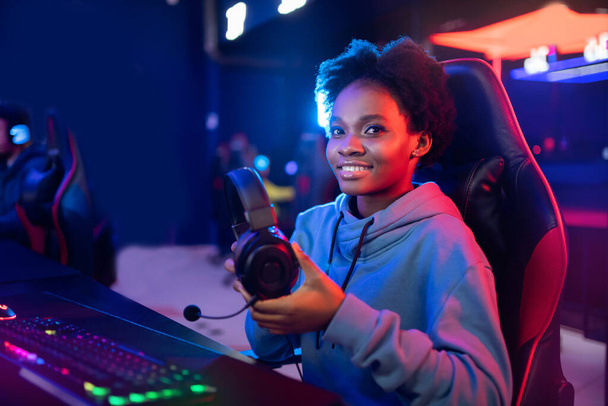 Jonge Afrikaanse gelukkige vrouw professionele gamer in online video game met hoofdtelefoon, neon achtergrond - Foto, afbeelding