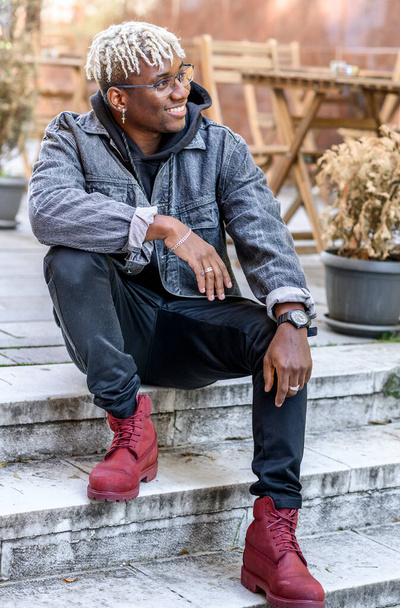 Sonriente hombre afroamericano con rastas se sienta en los escalones de afuera. Melinial de generación joven - Foto, Imagen