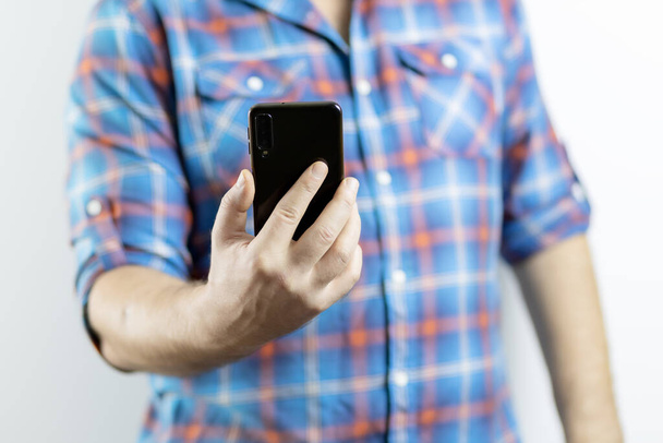 A man in a plaid shirt holds a mobile phone. Hand with phone in focus - Foto, Bild