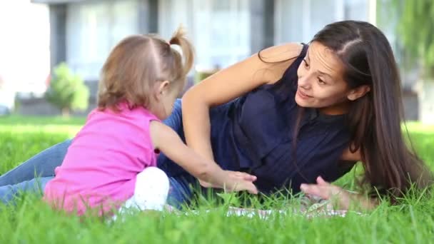 Nuori äiti vauvan kanssa kaupungin puistossa.Äiti leikkii vauvan kanssa puistossa nurmikolla.Perhe puistossa loma.Äiti, jolla on pieni tyttö luonnossa
. - Materiaali, video