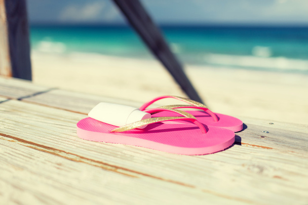 close up of sunscreen and slippers at seaside - Photo, Image