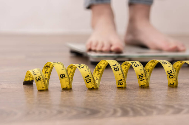 Female leg stepping on weigh scales with measuring tape. - Photo, Image