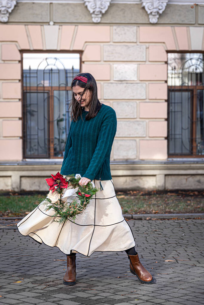 Stylish young woman with Christmas wreath outside, waiting for Christmas. - Foto, Bild
