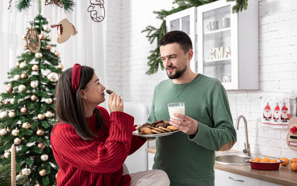 Boldog férj és feleség karácsonyi sütikkel és tejjel a konyhában. - Fotó, kép