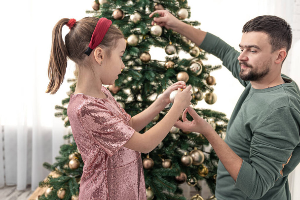Papá y su hijita decoran juntos el árbol de Navidad. - Foto, imagen