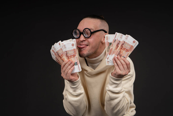 Young happy businessman dancing with a stack of money rubles isolated on black background. - Photo, Image