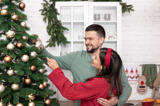 Happy married couple is decorating a Christmas tree on the eve of Christmas. - Photo, Image