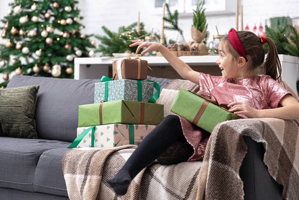 Una bambina gode di un sacco di regali di Natale seduti sul divano a casa. - Foto, immagini