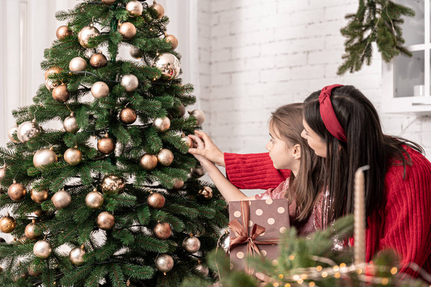 Mutter und kleine Tochter schmücken gemeinsam den Weihnachtsbaum. - Foto, Bild
