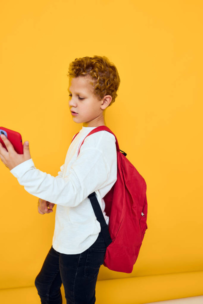 teenager chlapec v bílé mikině mobilní telefon červený batoh žluté pozadí - Fotografie, Obrázek