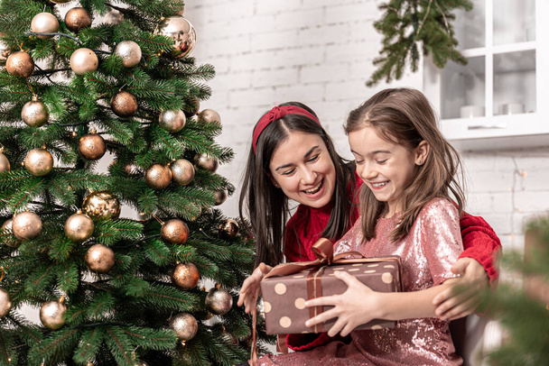 Anya egy kislánnyal a karácsonyfa mellett egy ajándékdobozzal.. - Fotó, kép