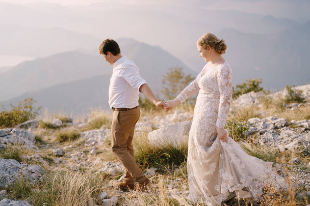 Жених и невеста спускаются с горы, держась за руки - Фото, изображение