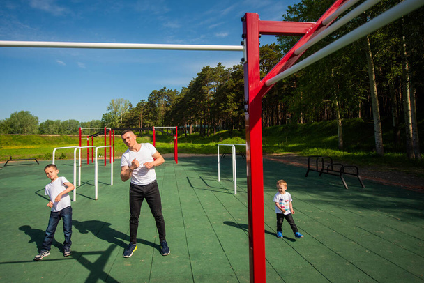 Caucasian man and two boys doing exercises outdoors. Father and sons train on the sports ground - Foto, Imagem