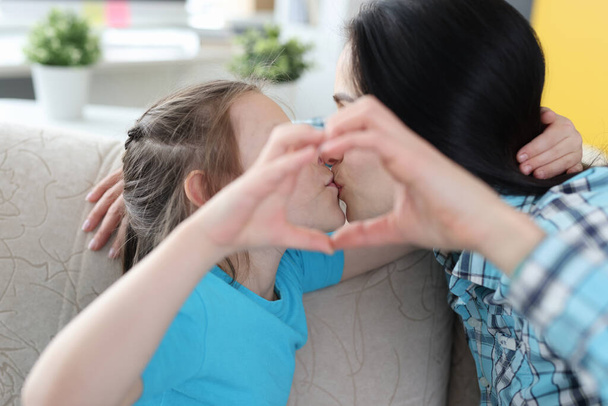 Mom kisses little daughter, together show heart gesture - 写真・画像