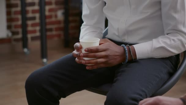 close-up van Afrikaans amerikaanse man fewling nerveus terwijl het houden van kopje koffie op aa vergadering - Video