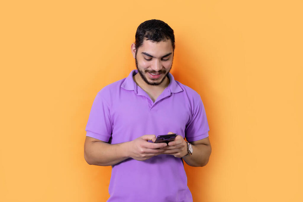 A young man with a beard, using his mobile phone posing in the orange background - Fotografie, Obrázek