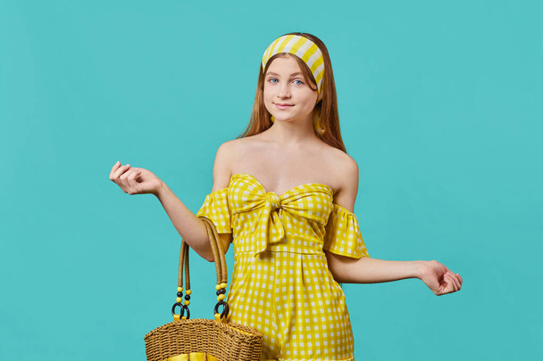 Portrait of a young girl in yellow summer clothes looking at camera over blue pastel background. - Foto, afbeelding