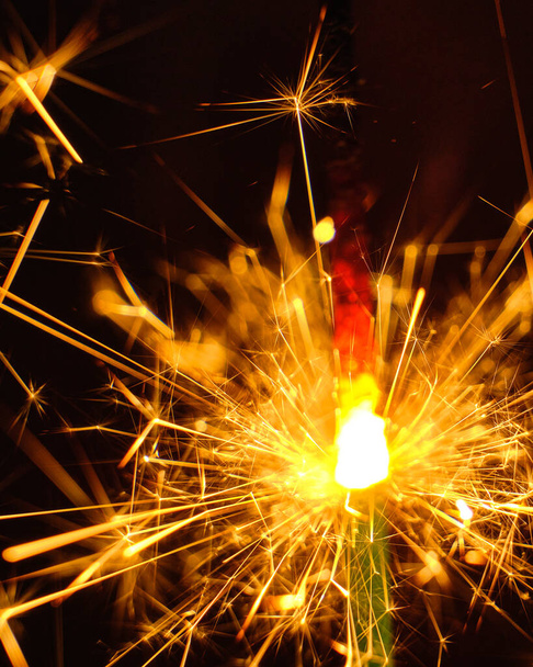 A close-up shot of a burning sparkling bright firework stick in the darkness - Foto, Imagen