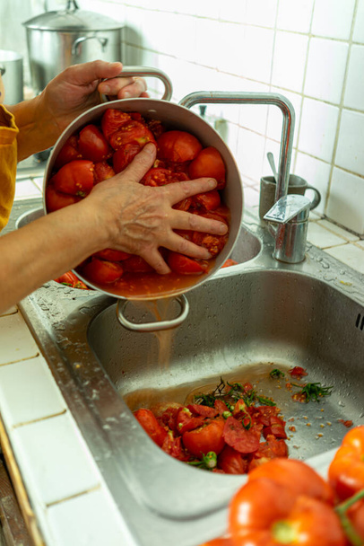 A vertical shot of an elderly lady squeezing the water of a pot with boiled tomatoes into the sink - Photo, image