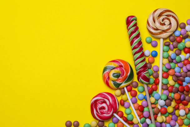 Delicious lollipops and candies on yellow background, flat lay. Space for text - Foto, imagen