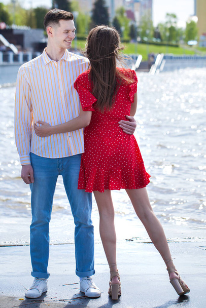 Ο νεαρός αγκαλιάζει την κοπέλα του με κόκκινο φόρεμα. - Φωτογραφία, εικόνα