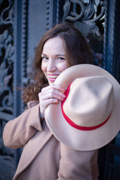 Portrait of smiling pretty woman with curly hair near the old door with a hat - Foto, imagen