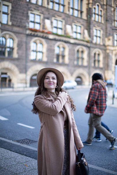 Pretty woman with curly hair in old town dressed in autumn coat and a hat - 写真・画像
