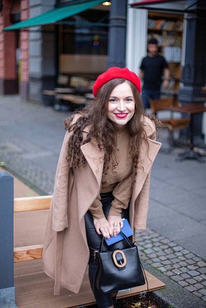 Smiling pretty woman with curly hair in red french beret walking in the street - 写真・画像