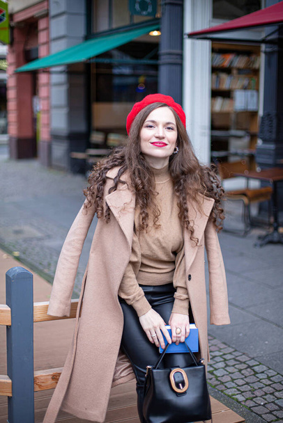 Smiling pretty woman with curly hair in red french beret walking in the street - Photo, image