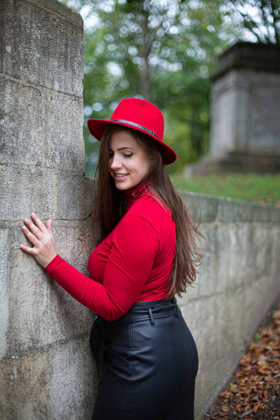 White woman with long dark hair in bright red touching stone wall in autumn park - Foto, immagini